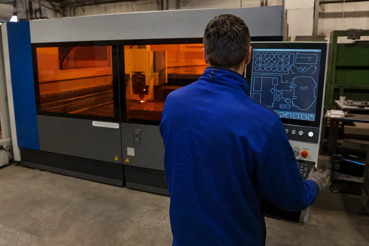 Opérateur consultant un écran de commande numérique devant une machine de découpe laser en cabine